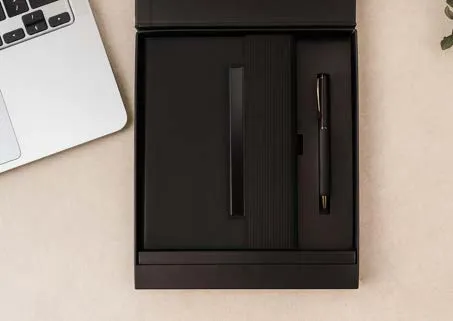 Black ribbed-cover diary with black pen in an open black gift box beside a laptop