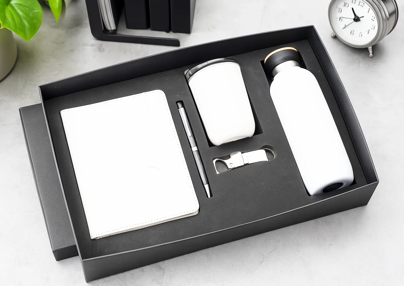 White diary, pen, coffee tumbler, bottle opener and vacuum flask arranged in a black gift box.