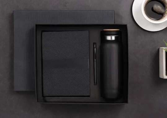 Black gift box with a herringbone diary, a pen and a bamboo-capped flask beside a cup of coffee.