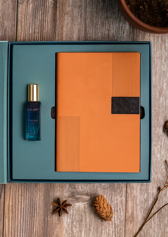 Teal gift box holding a tan-orange notebook, card holder, keychain, pen and a blue fragrance bottle.