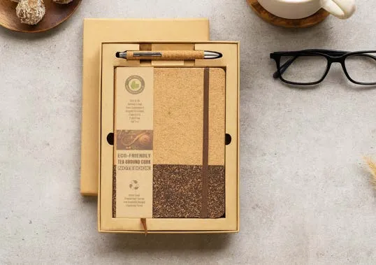 Eco-friendly tea-ground cork diary with elastic strap and cork pen in a kraft box beside glasses and coffee.