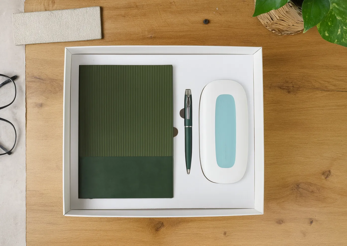 White gift tray holding a green ribbed diary, dark green metal pen and a white foldable LED desk lamp with teal panel on a wooden desk.