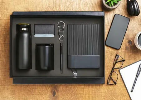 Black JoyBox 6-in-1 gift set with bottle, tumbler, keychain, pen, card holder and ribbed diary on wood.