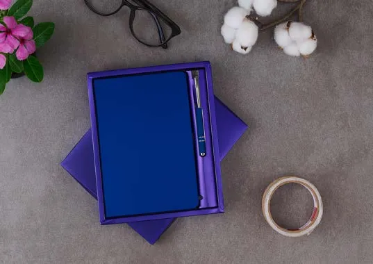 Royal-blue diary with slim pen in a purple gift box on a grey surface