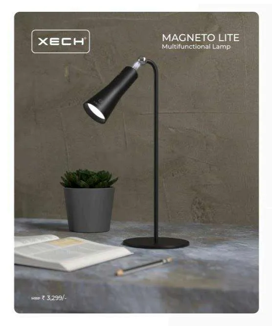 Black XECH Magneto Lite desk lamp beside a potted plant and open book on a stone surface.