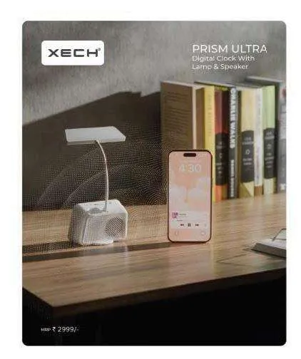 White XECH Prism Ultra desk lamp and clock speaker with a phone propped in its base stand against a bookshelf.