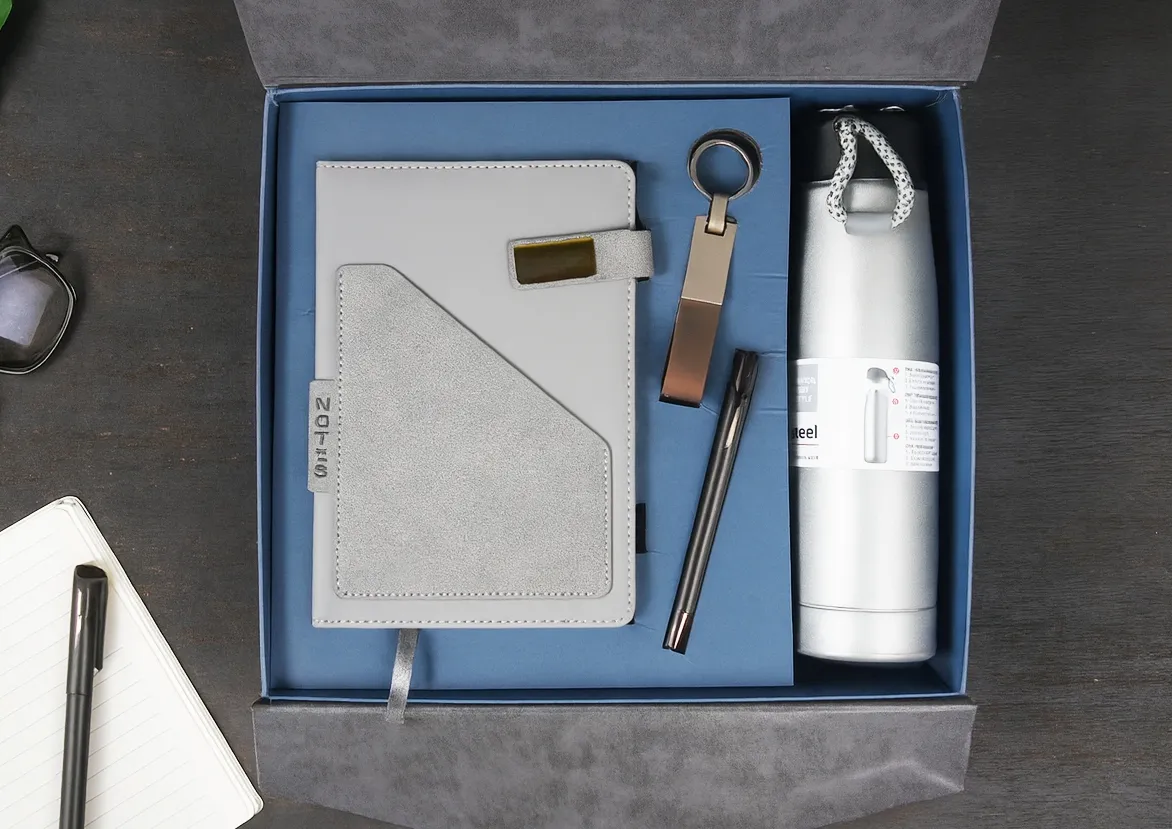 Open grey gift box holding a grey leatherette diary, metal keychain, metal pen and a silver steel vacuum flask.