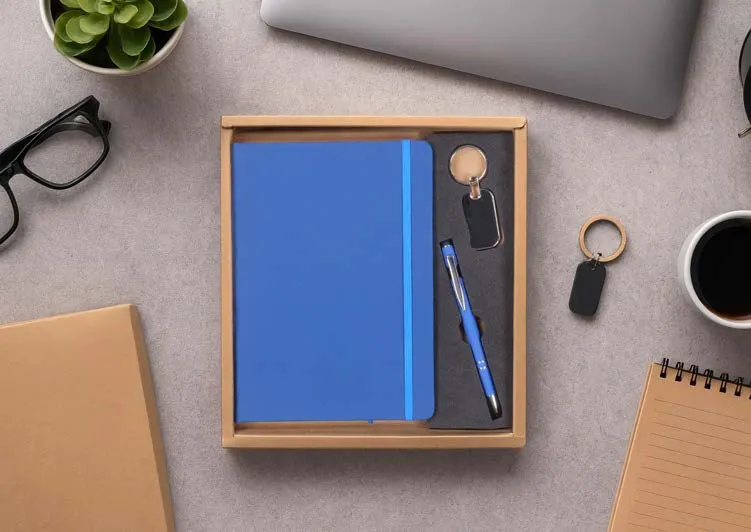 Blue A5 diary, matching pen and metal keychain in a natural kraft gift tray on a desk.
