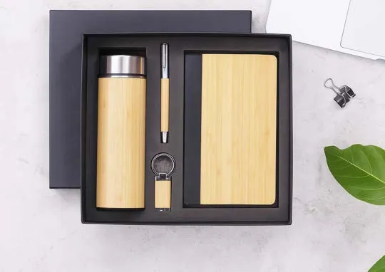 Black gift box with bamboo-finish flask, bamboo-cover diary, bamboo pen and keychain on a stone surface