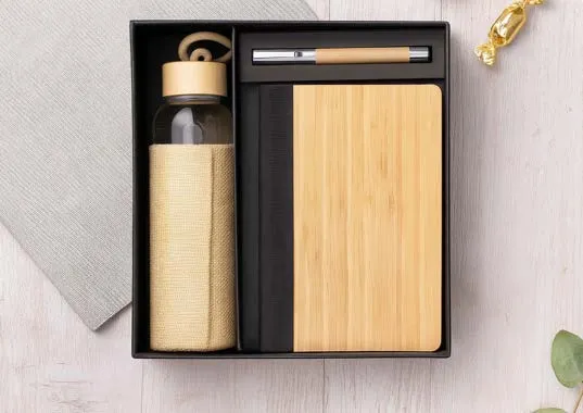 Black tray holding a jute-sleeved glass bottle with bamboo lid, a bamboo diary and a pen