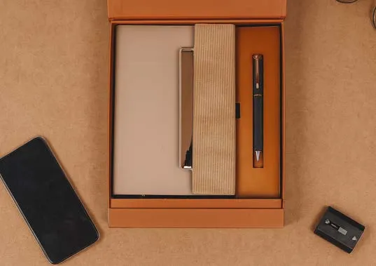 Tan diary with textured band and black pen in an orange-lined gift box beside a phone