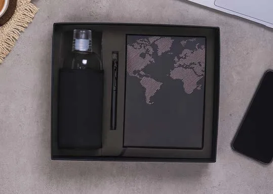 Black gift box with glass bottle in sleeve, slim pen and a world-map hardcover diary.
