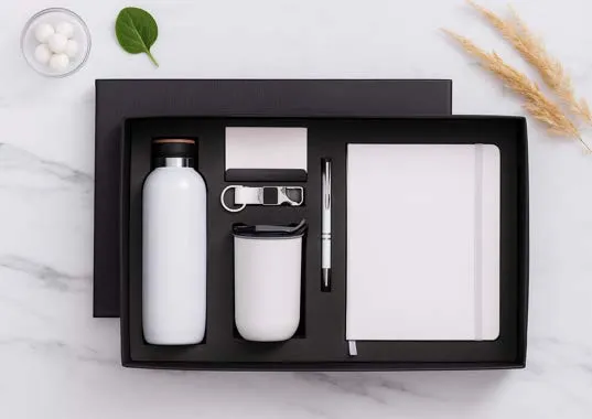 White 6-in-1 gift set with bottle, tumbler, keychain, pen and diary in a black box on marble.