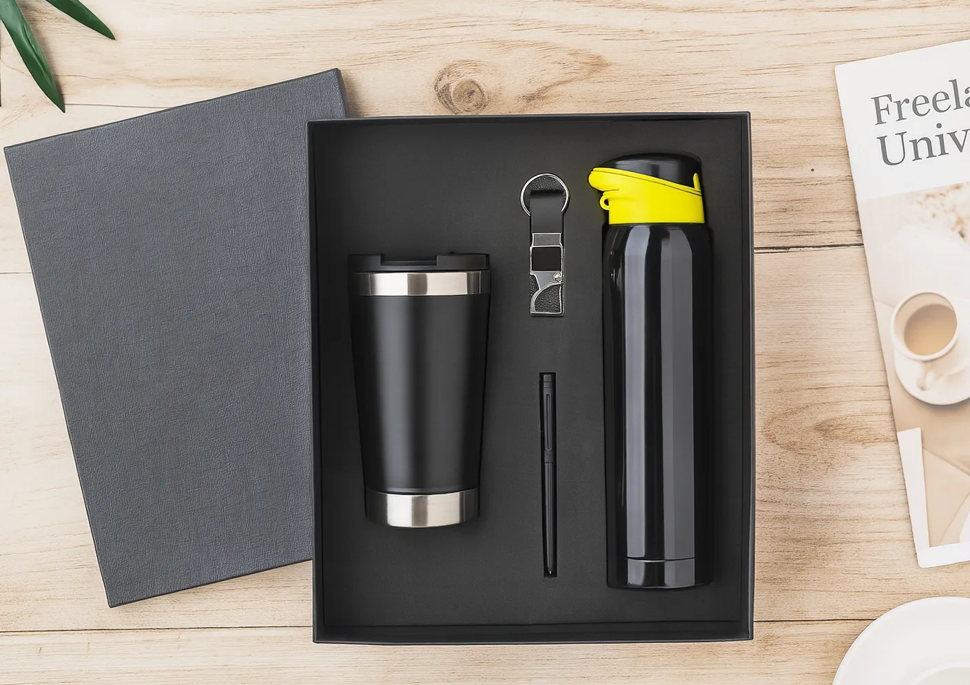 Black gift set with steel tumbler, metal pen, keychain and yellow-lidded vacuum bottle in a black tray beside a grey diary.