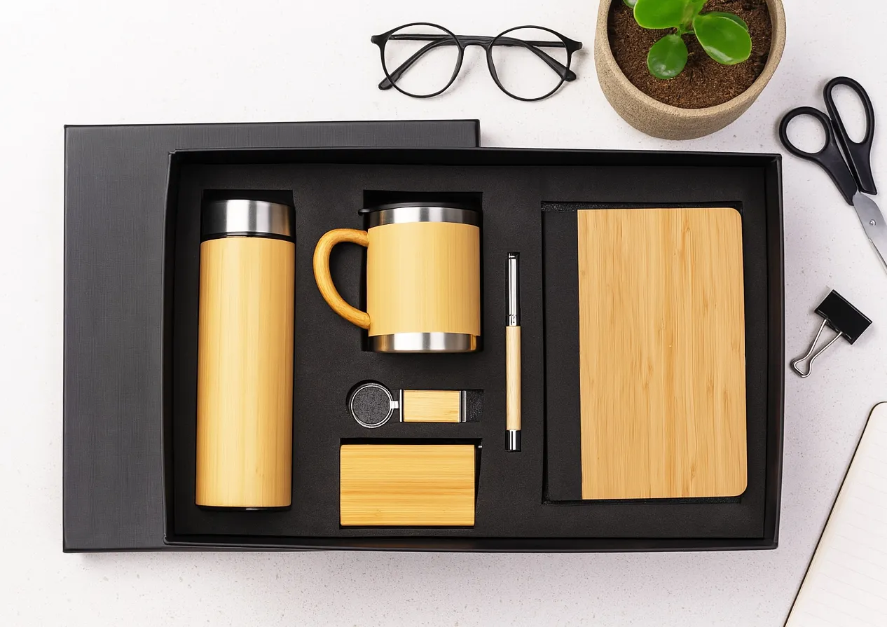 Black gift box holding bamboo-finish flask, mug, pen, keyring, USB and diary on a desk.